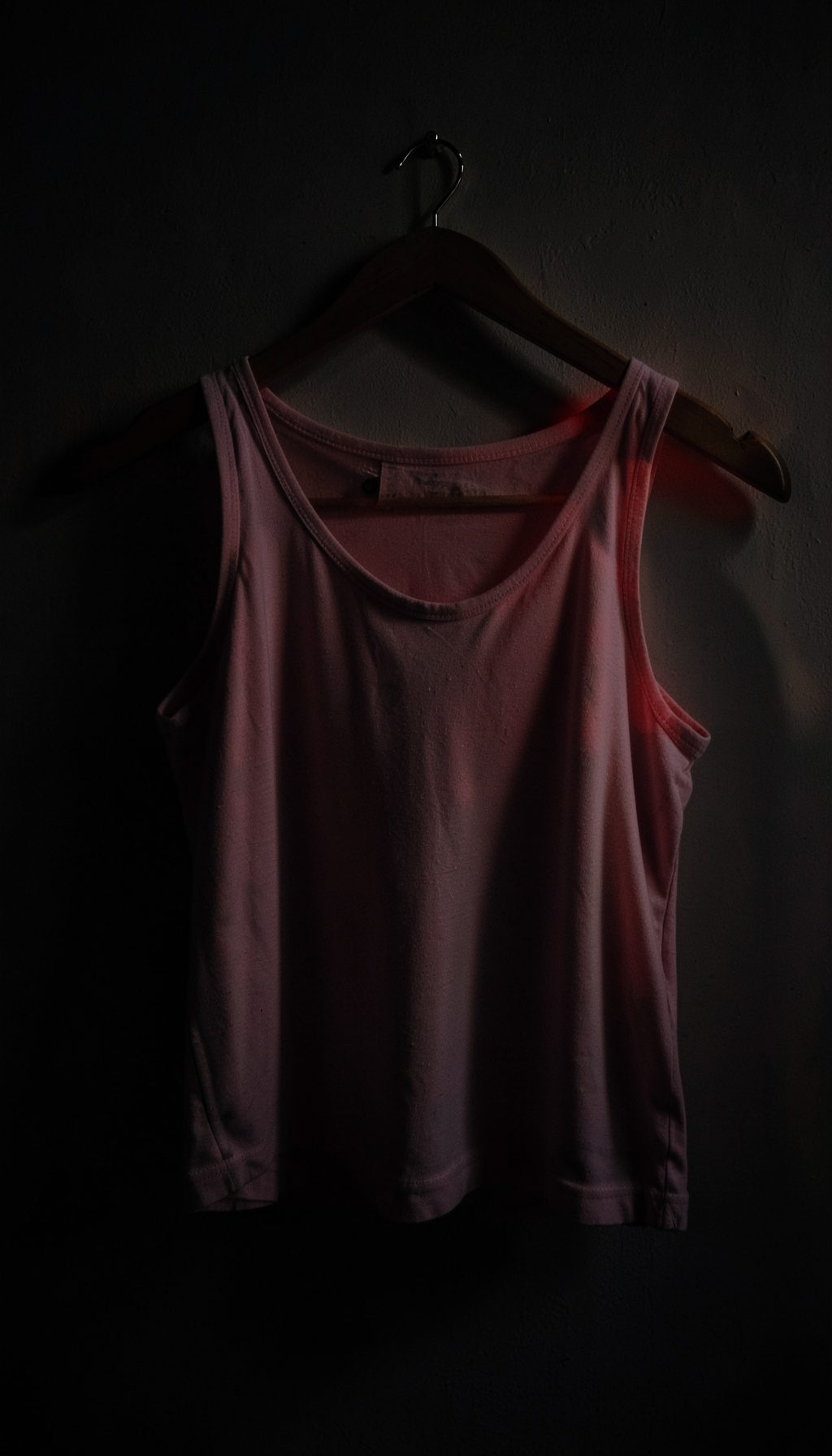 Dark moody shot of a pastel girls' top draped over a wooden hanger against a shadowed wall