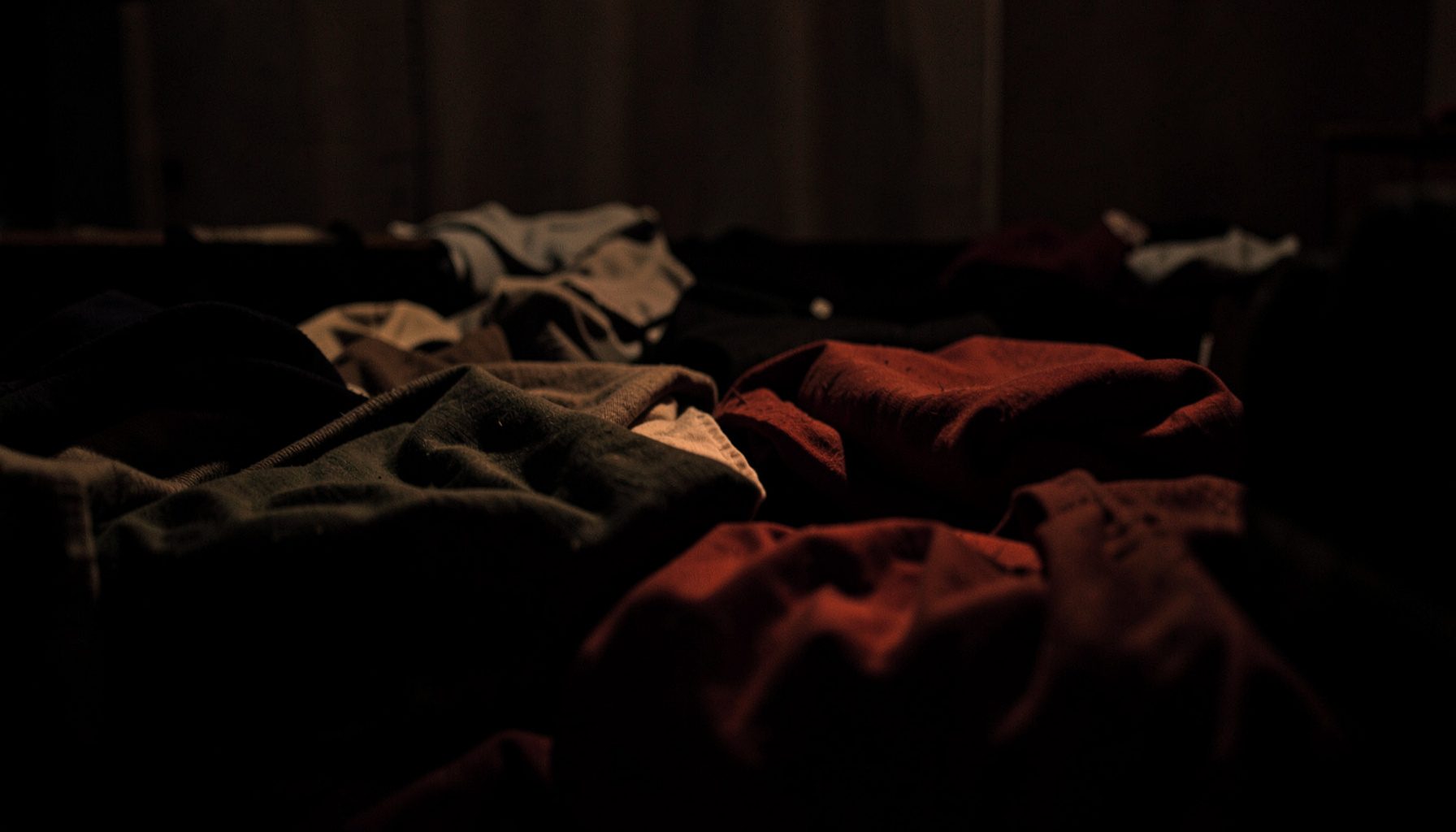 Dark textile workspace with folded garments in deep shadow, warm muted tones